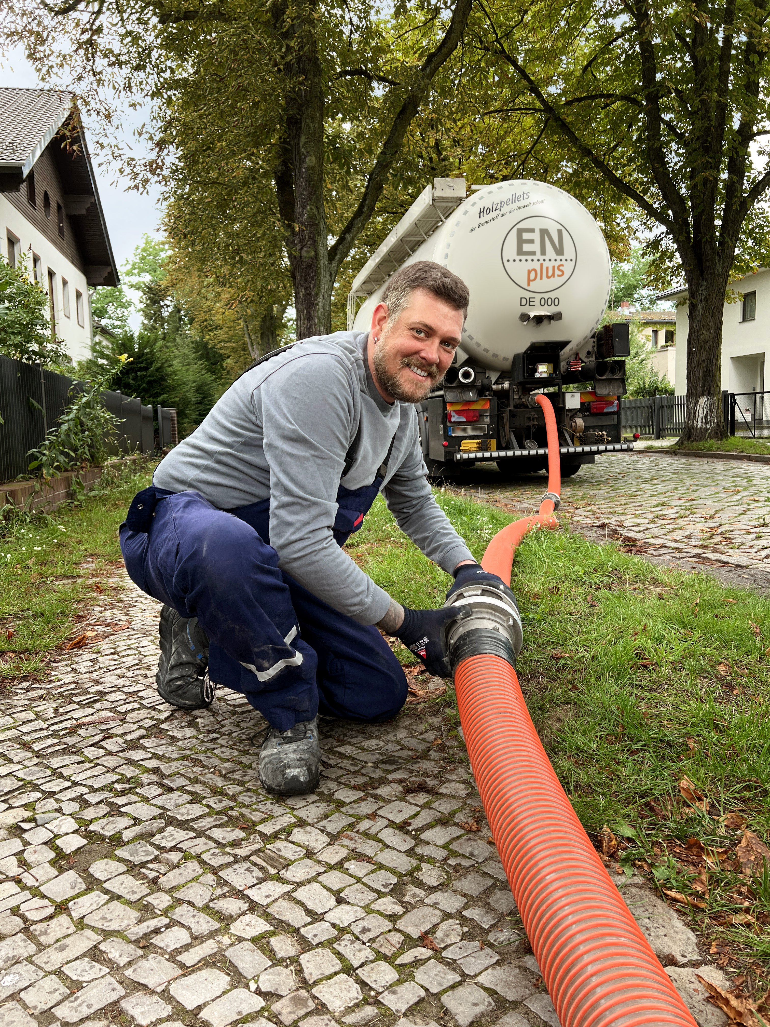 Pelletlieferant kniet vor einem LKW und schraubt roten Schlauch zusammen