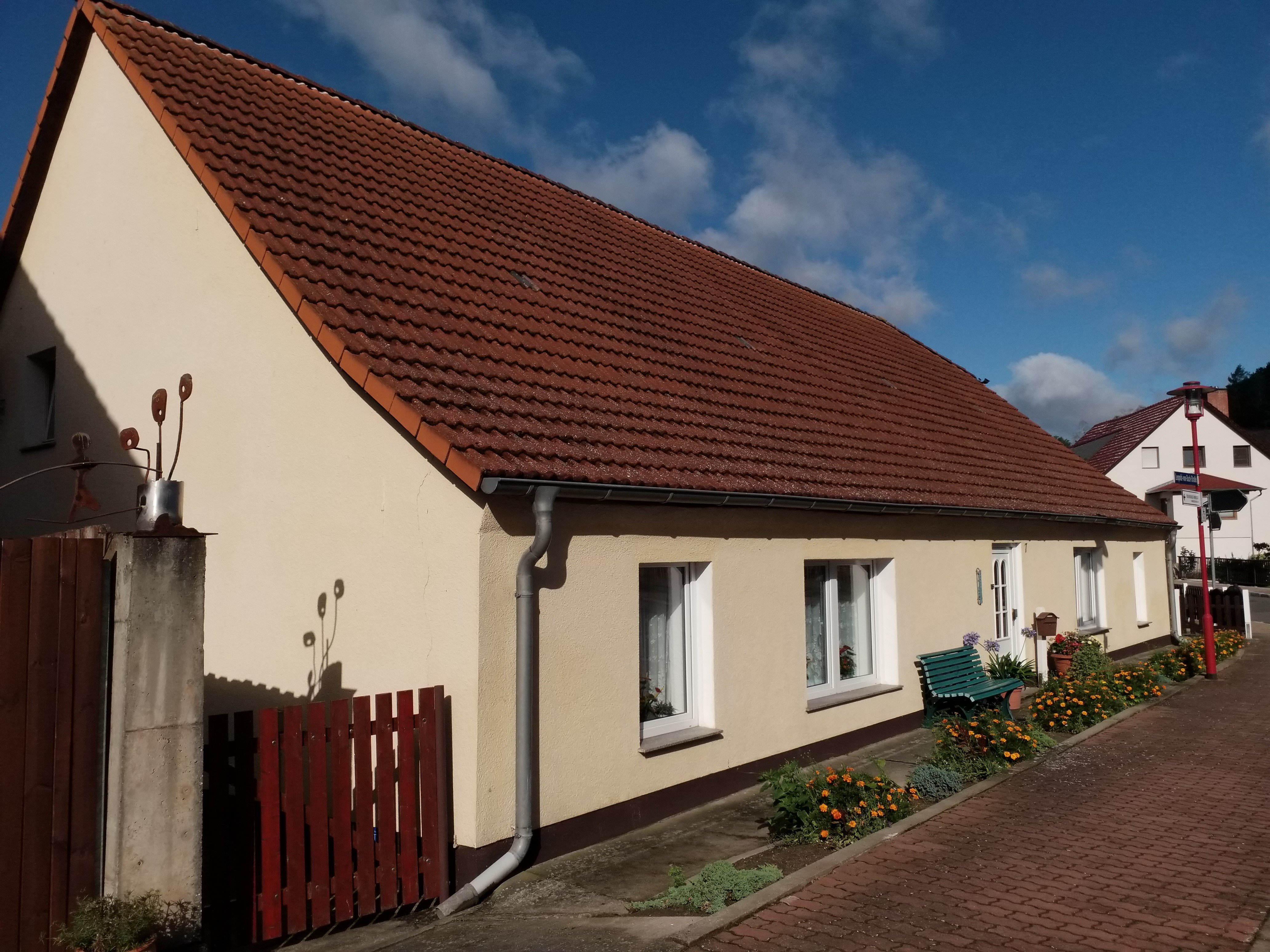 Das Bild zeigt ein gelbes Wohnhaus mit einem kleinen Vorgarten, daneben ist ein weißes Haus und im Hintergrund ein blauer Himmel zu sehen.