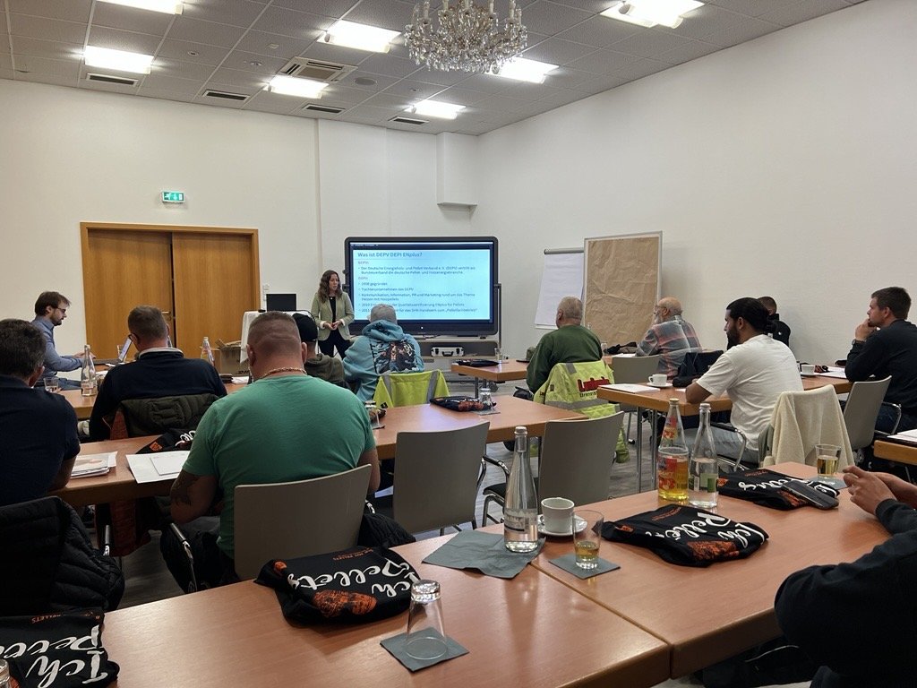 Das Bild im Querformat zeigt einen Schulungsraum mit einer Frau, die anhand einer Präsentation den Schulungsteilnehmern etwas erklärt.