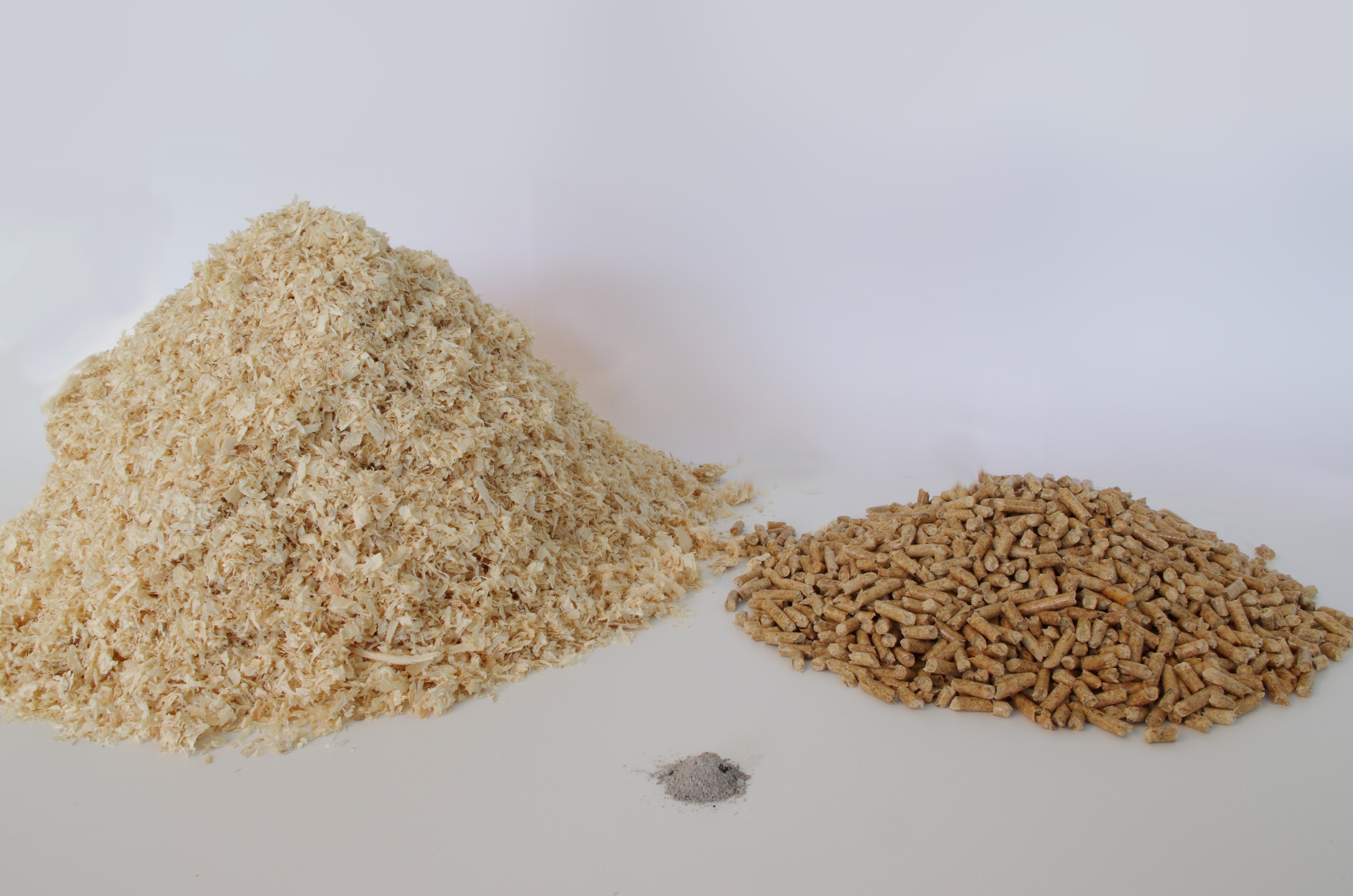 Links ein Haufen Sägespäne. Rechts daneben ein Haufen Pellets, der halb so groß ist, wie der Haufen aus Sägespänen. Und vorne in der Mitte ein Haufen Asche, im Vergleich zu den anderen Haufen deutlich kleiner.