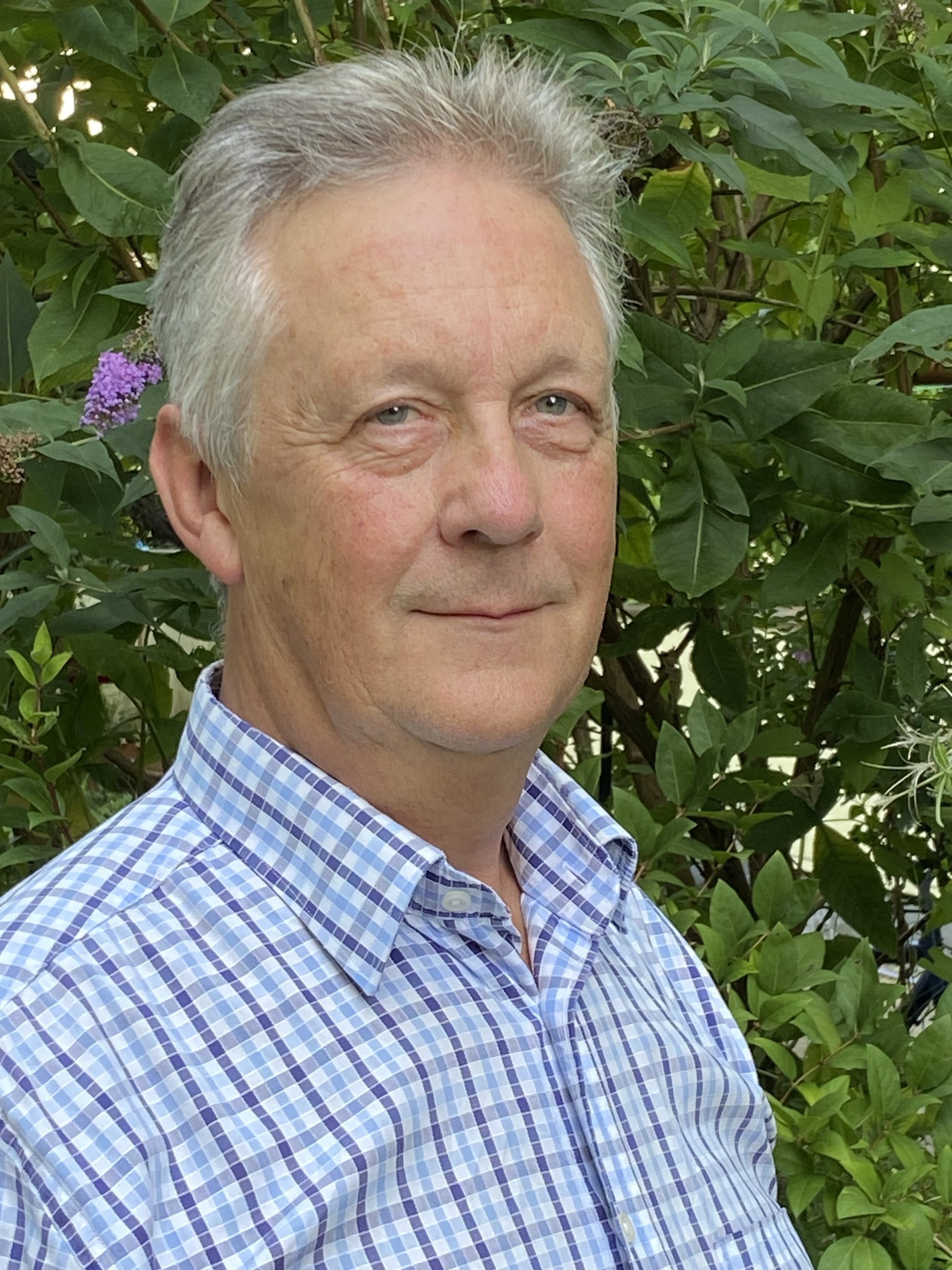 Das Bild zeigt ein Foto von Harald Ruschenburg vor einer grünen Hecke.