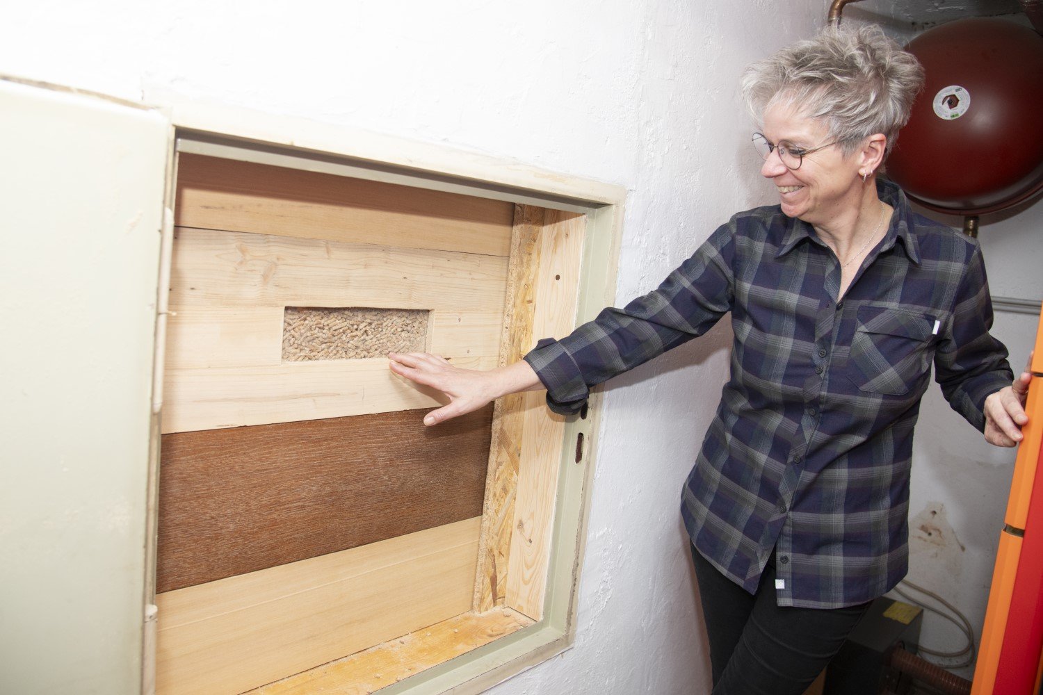 Eine weibliche Person steht neben einer Zugangsöffnung, zu einem Pelletlager. Durch eine Lucke sind Pellets erkennbar.
