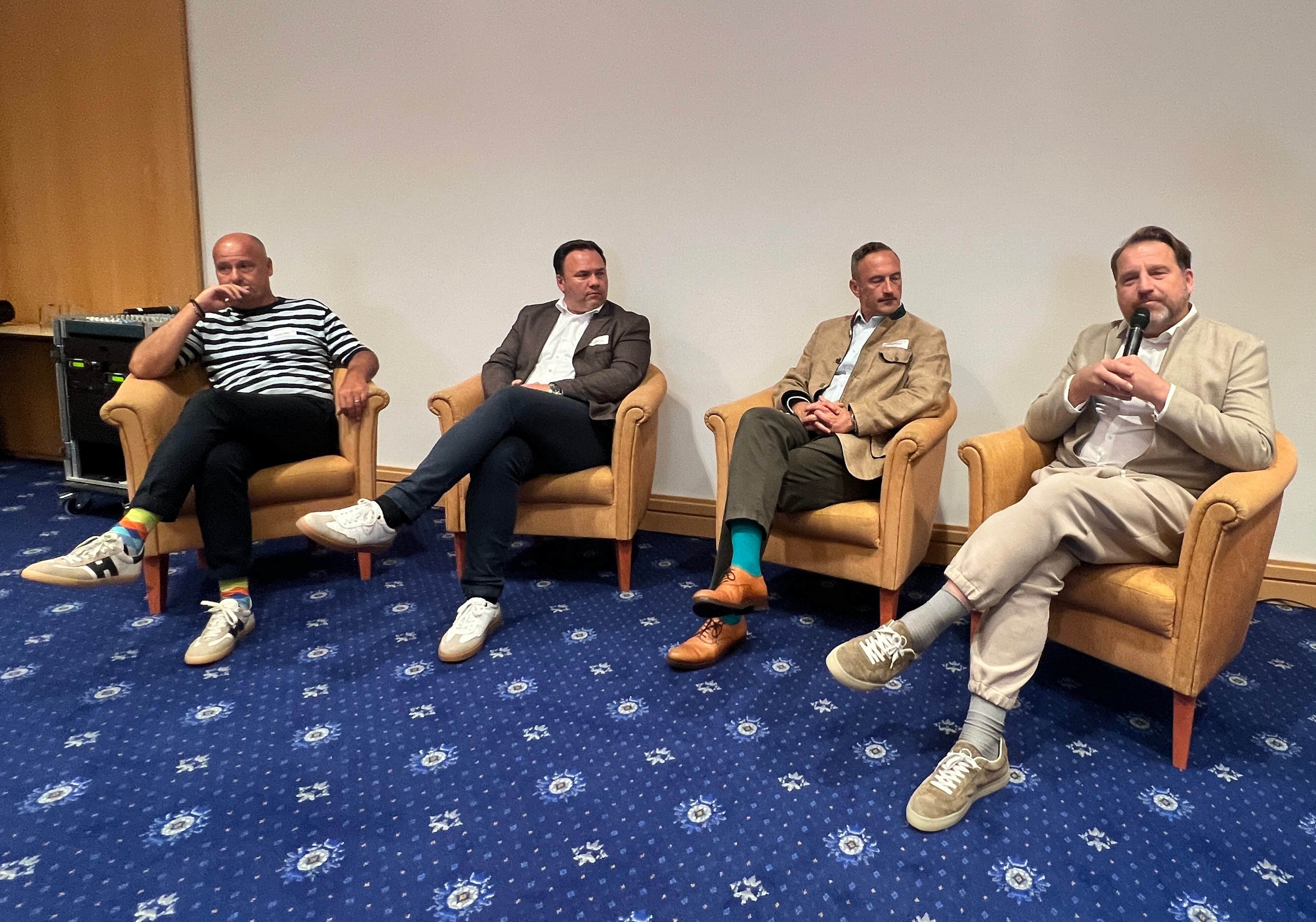 Vier Männer sitzen in Sesseln für eine Diskussionsrunde